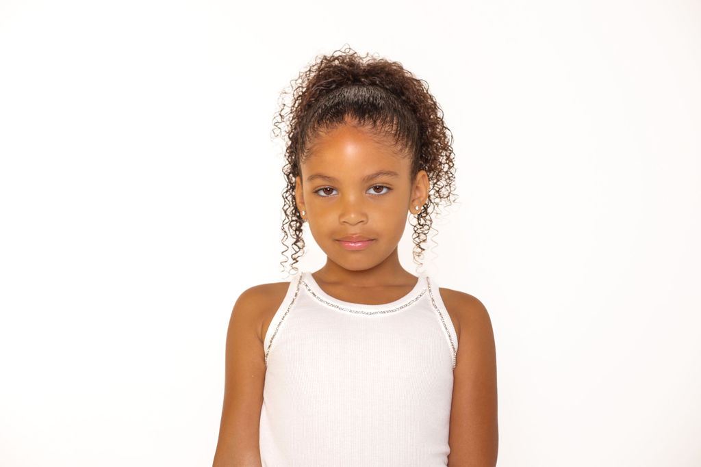 Studio headshot of a child in a white tank, hair in a high ponytail
