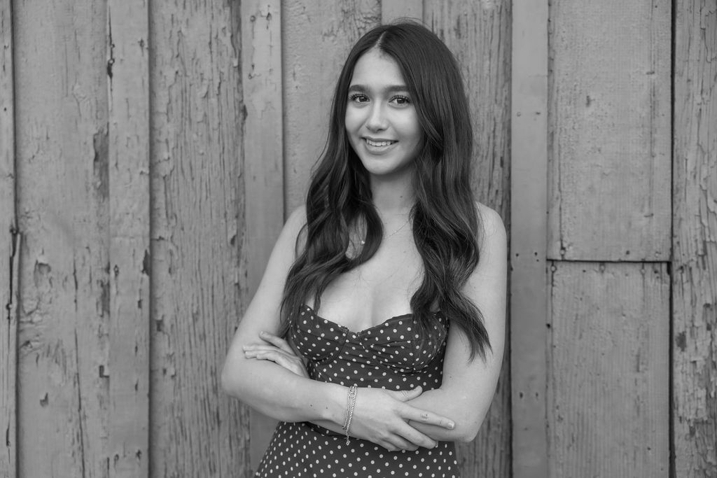 Black-and-white outdoor portrait against weathered wood in a polka-dot dress